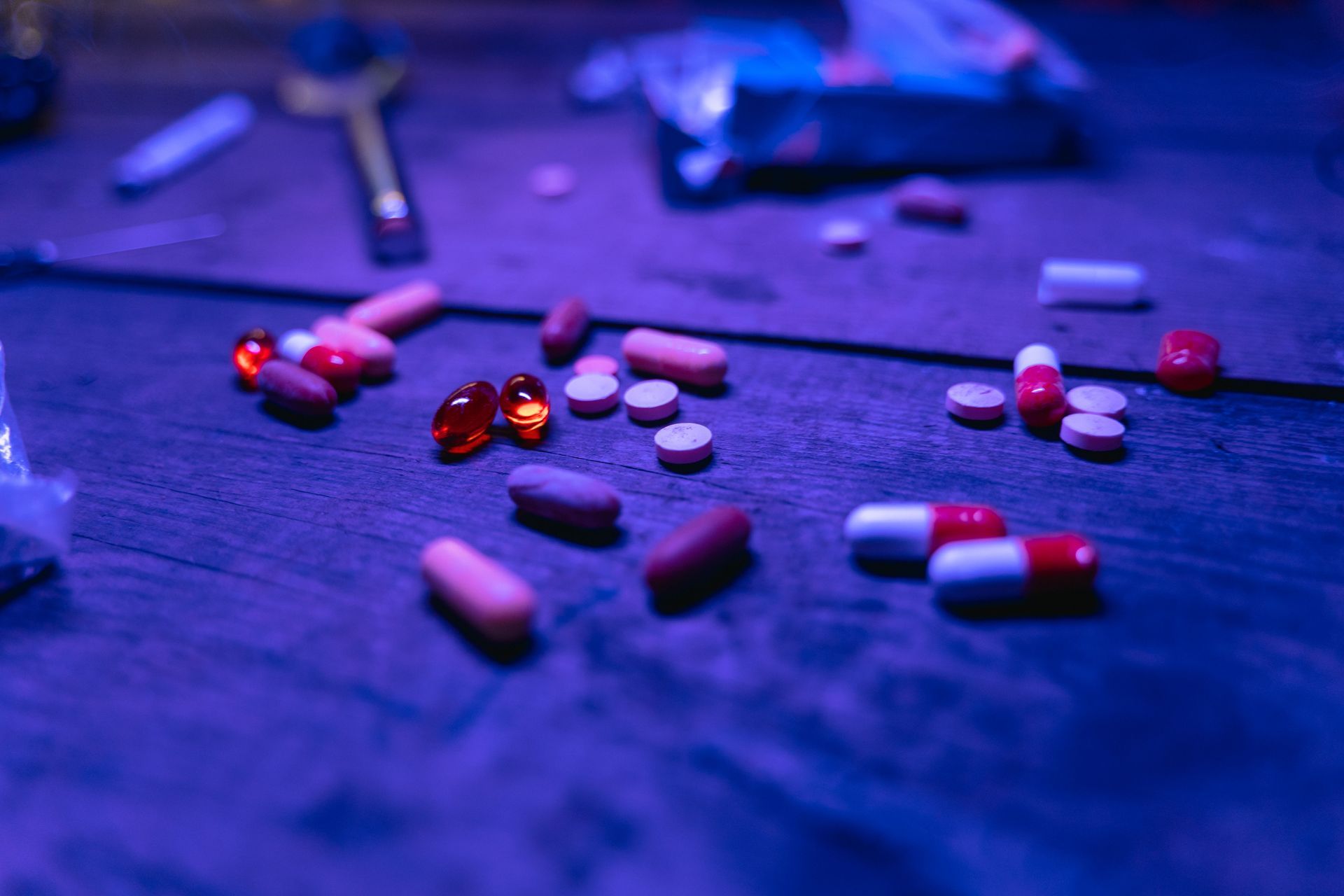 Scattered red, pink, and white capsules and tablets on a purple-lit surface