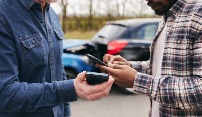 Two people comparing smartphones outdoors beside a parked car