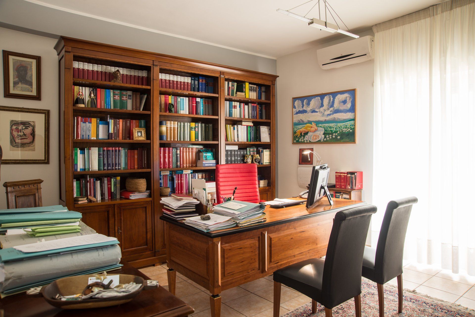Una stanza con una scrivania, sedie, librerie e una finestra.