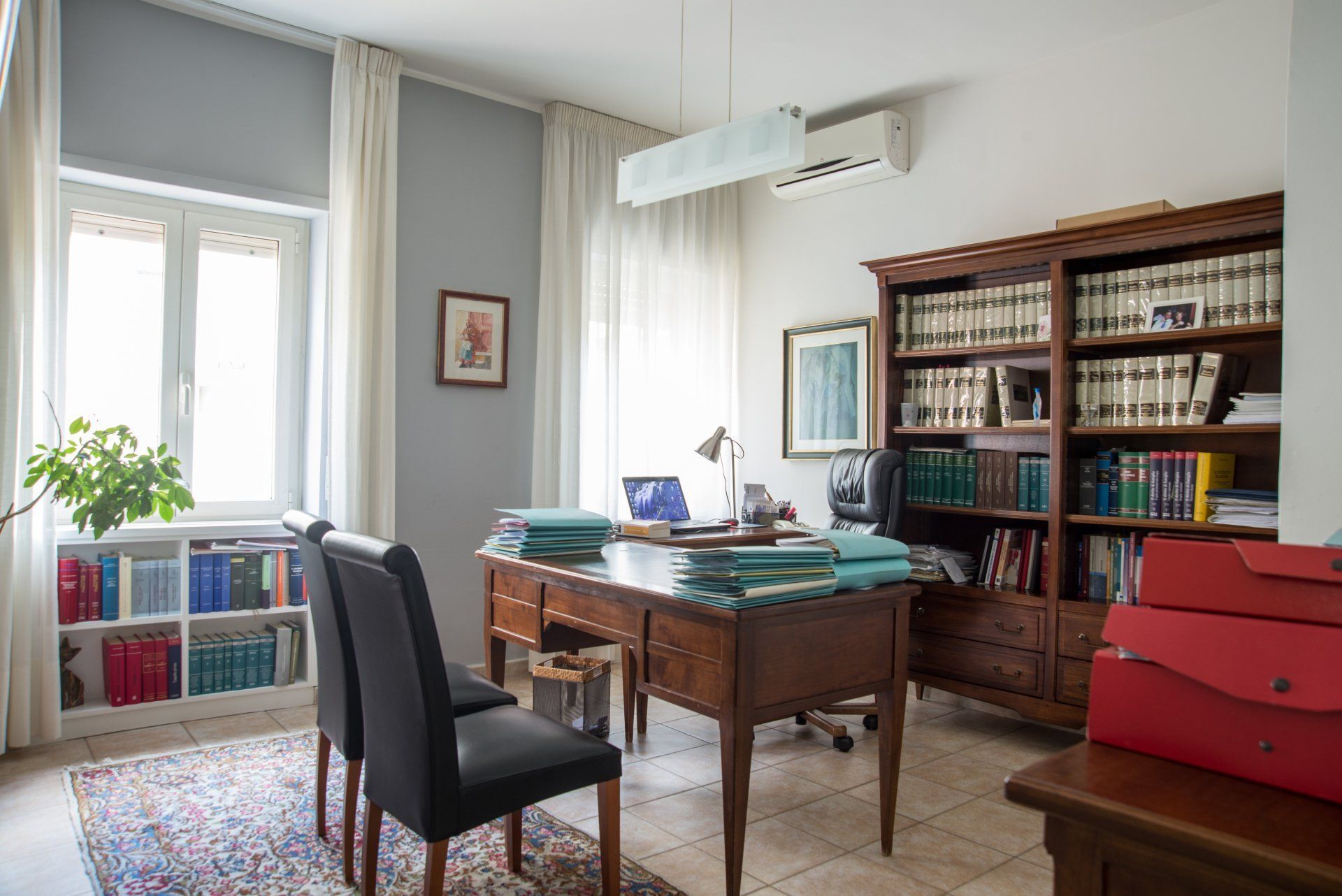 Una stanza con una scrivania, sedie, librerie e una finestra.