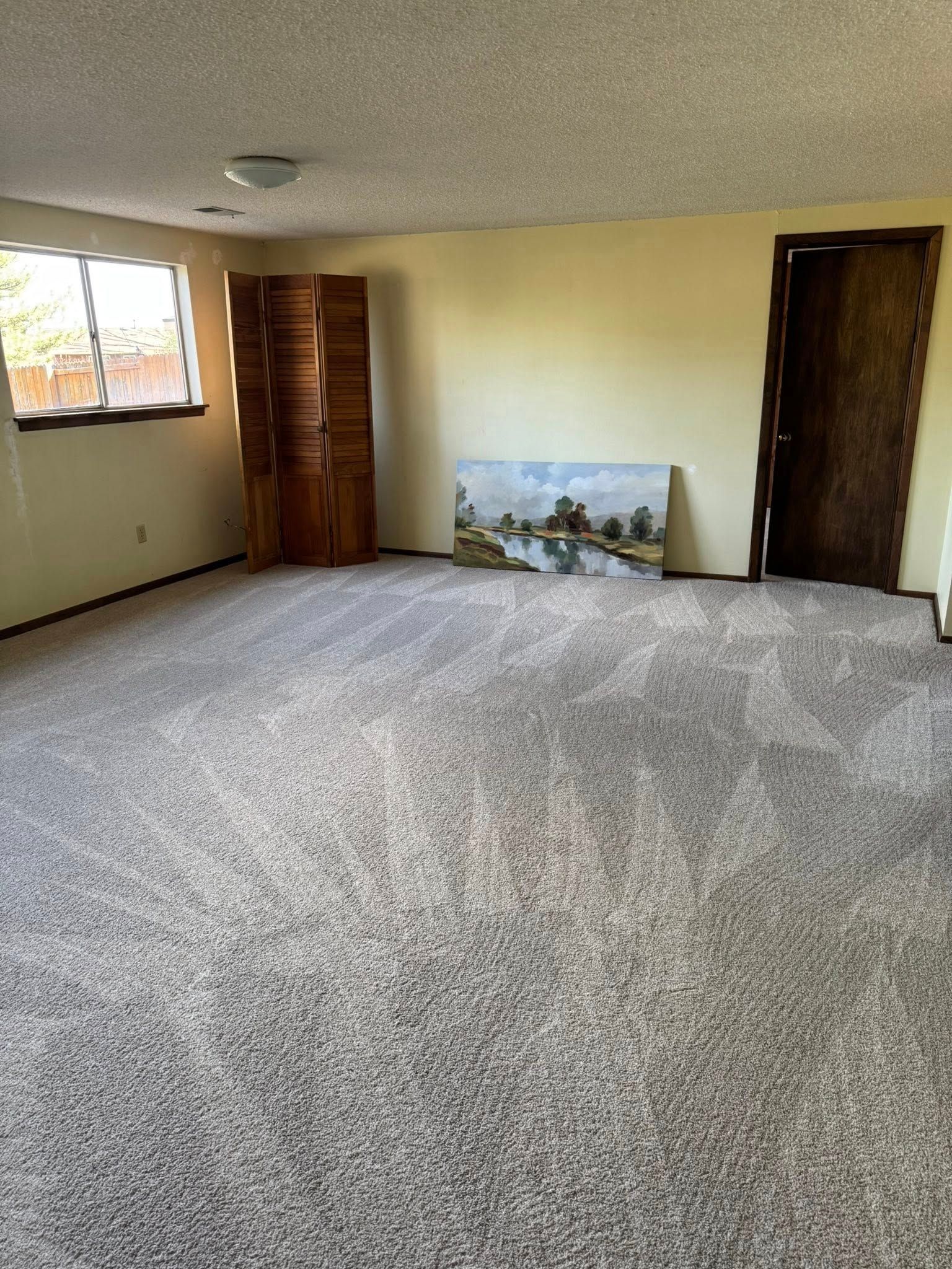 Empty room with beige walls, gray carpet, a painting, and a folding screen.