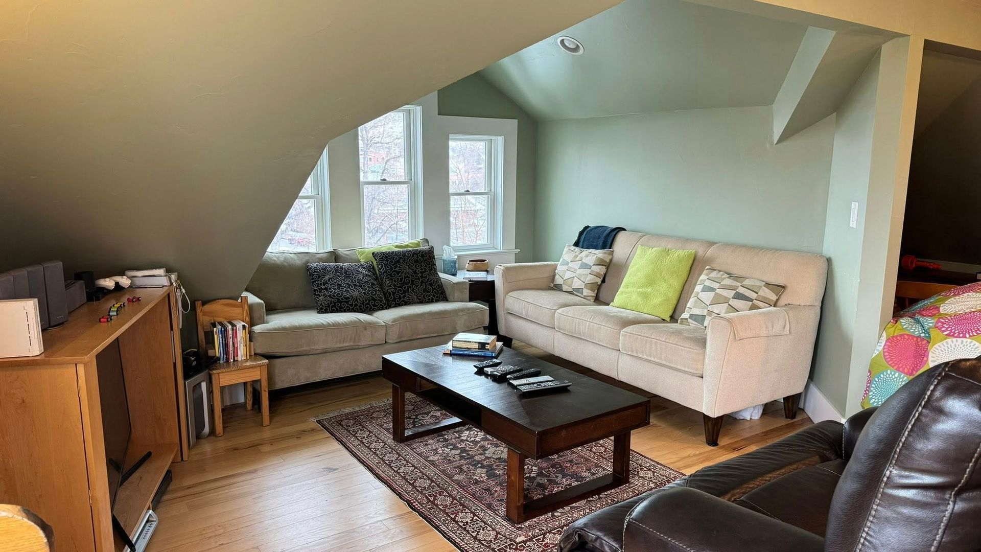 Living room with sofas, coffee table, and bookshelves; natural light from windows.