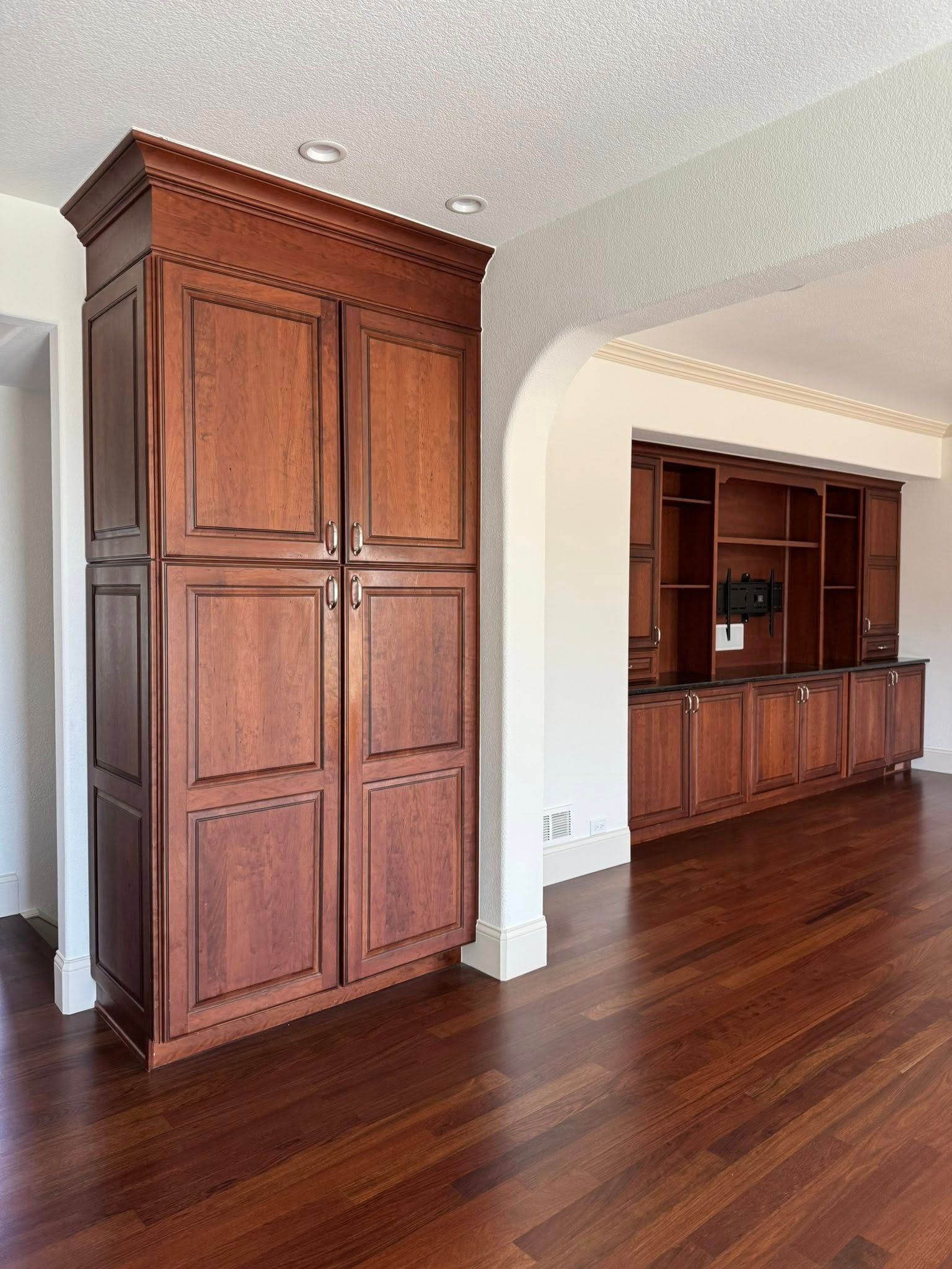 Dark wood cabinets in a room with wood flooring, adjacent to arched doorway.