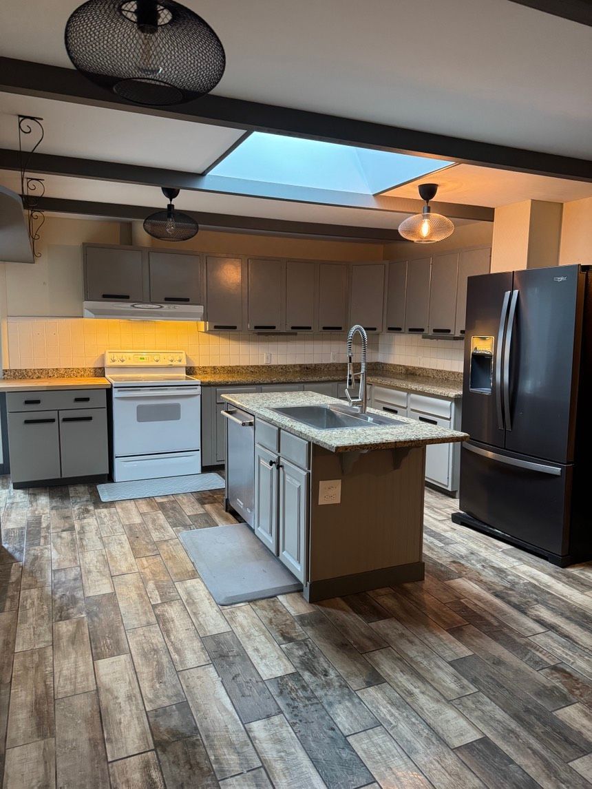 Modern kitchen with gray cabinets, island, and stainless steel appliances. Hardwood flooring and skylight.