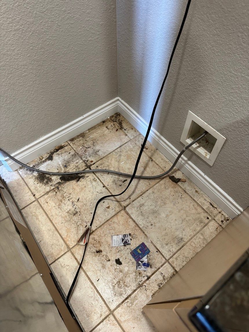 Dirty floor with black cords, electrical outlet, and off-white trim. Debris scattered on the tile.