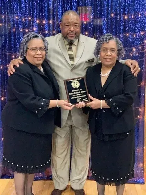 Three people holding a plaque on a stage with blue lights, smiling at the camera.