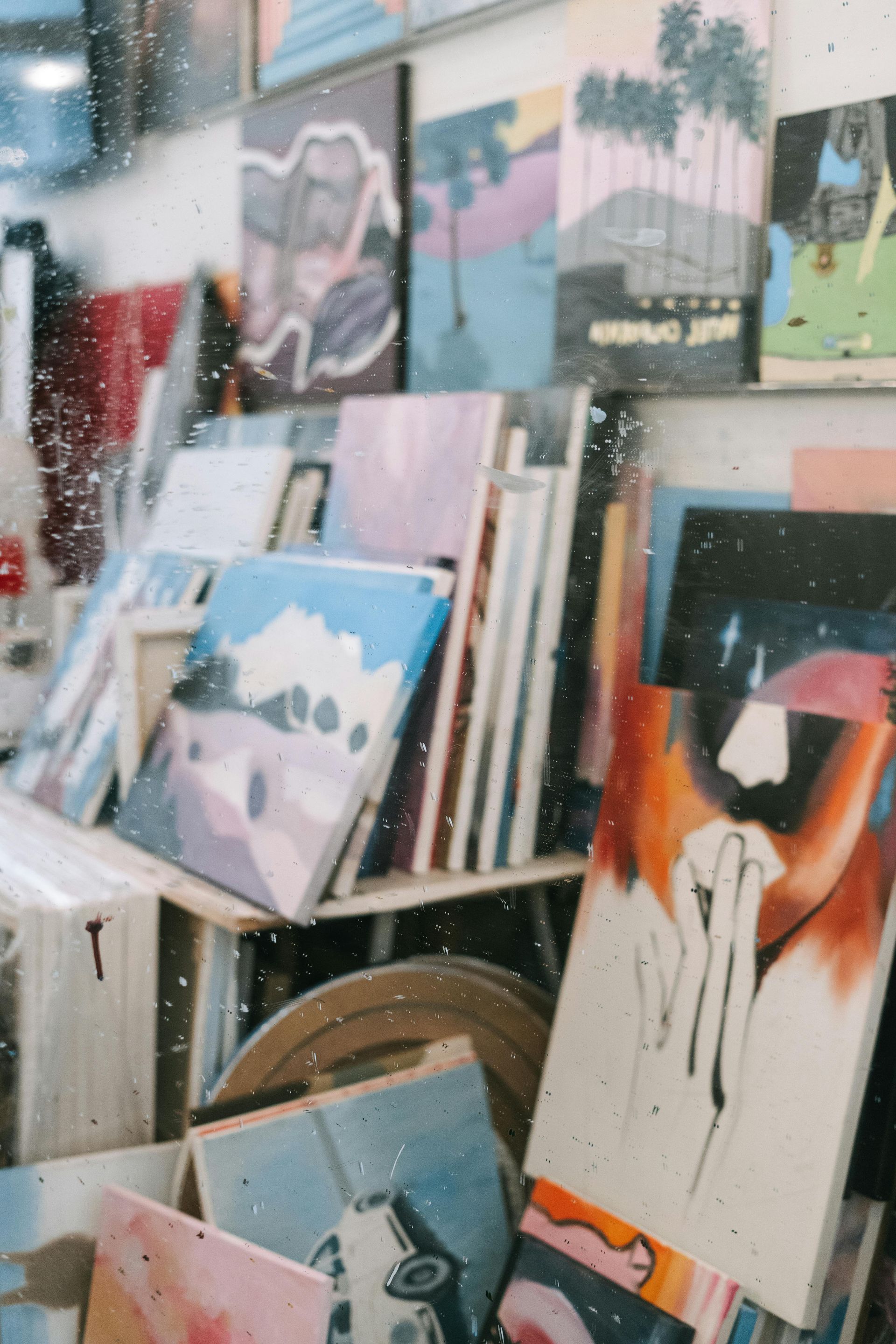 Assorted abstract paintings and canvases stacked in a studio, with colorful artwork leaning on shelves.