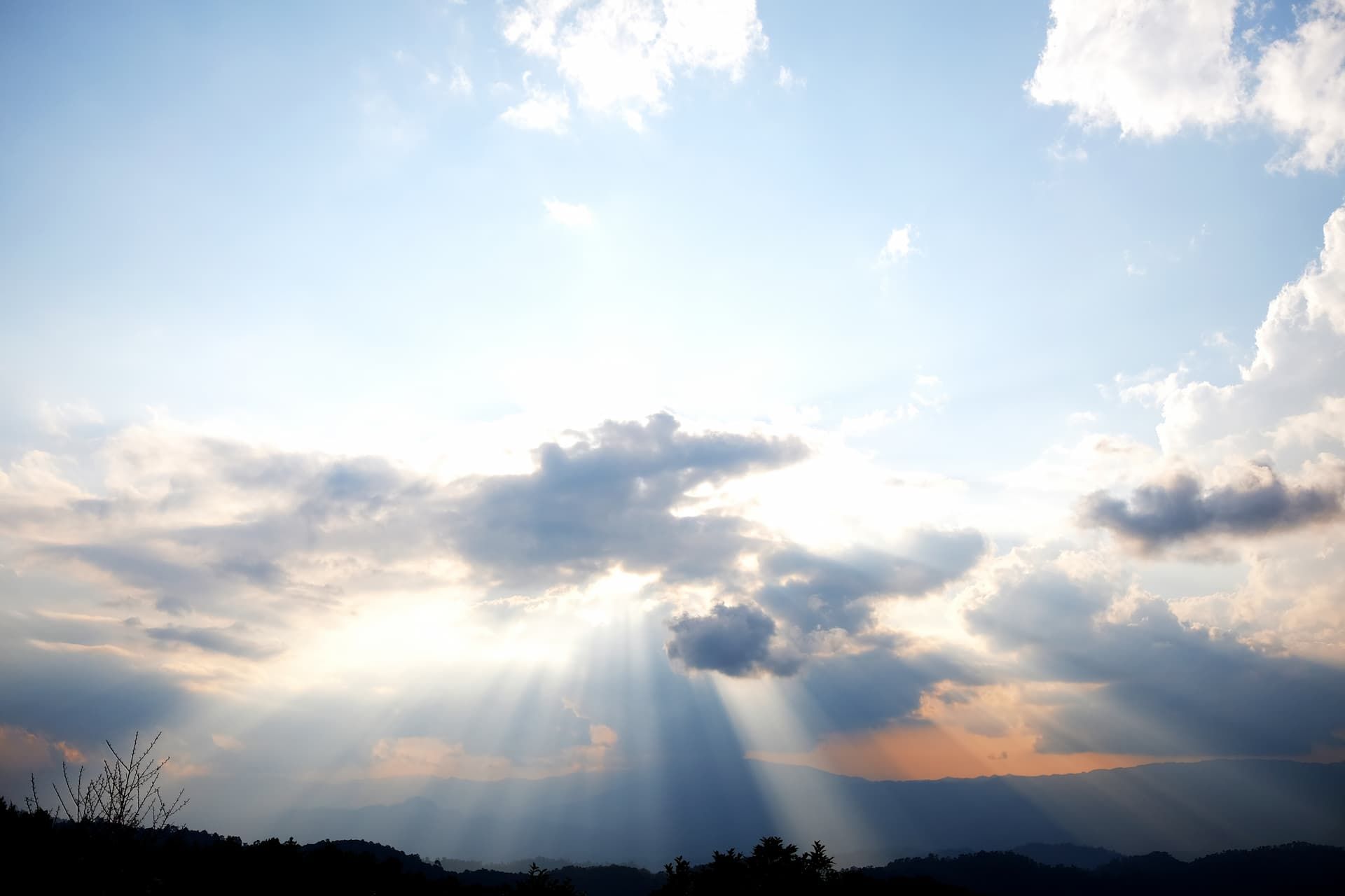 Sun rays breaking through clouds over a dark mountain ridge at sunset