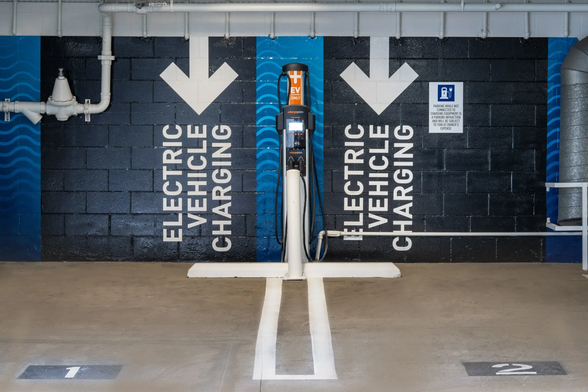 Electric vehicle charging station in parking garage with arrows and text at The Preston in Los Angeles, CA.