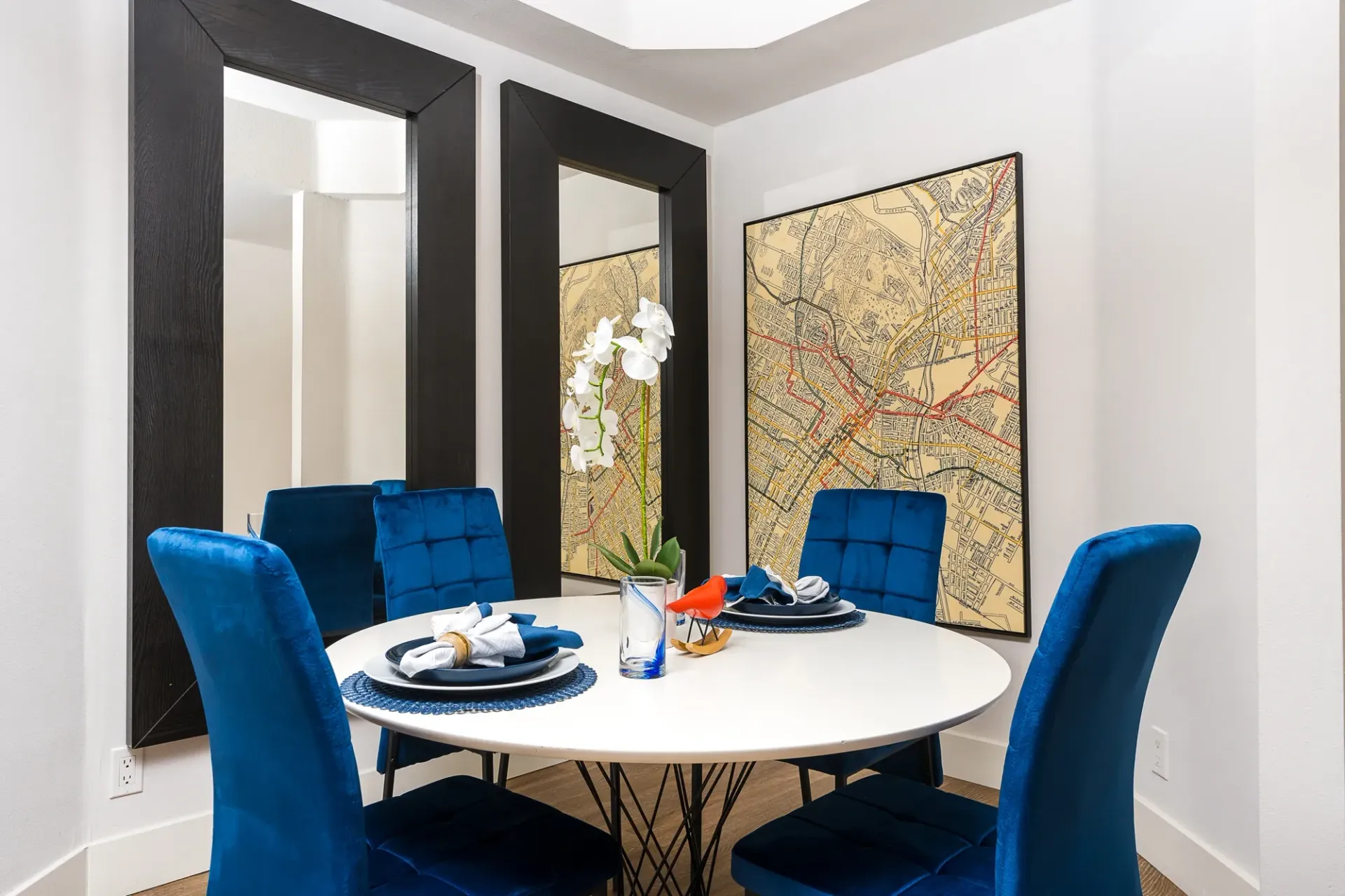 Dining area with a round table, blue chairs, and a map art at The Preston in Los Angeles, CA.
