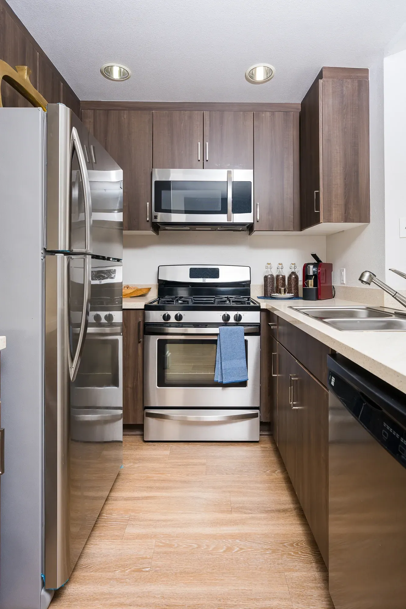Stainless steel gas range and microwave above, with dark wood cabinetry and a side-by-side refrigerator at The Preston in Los Angeles, CA.