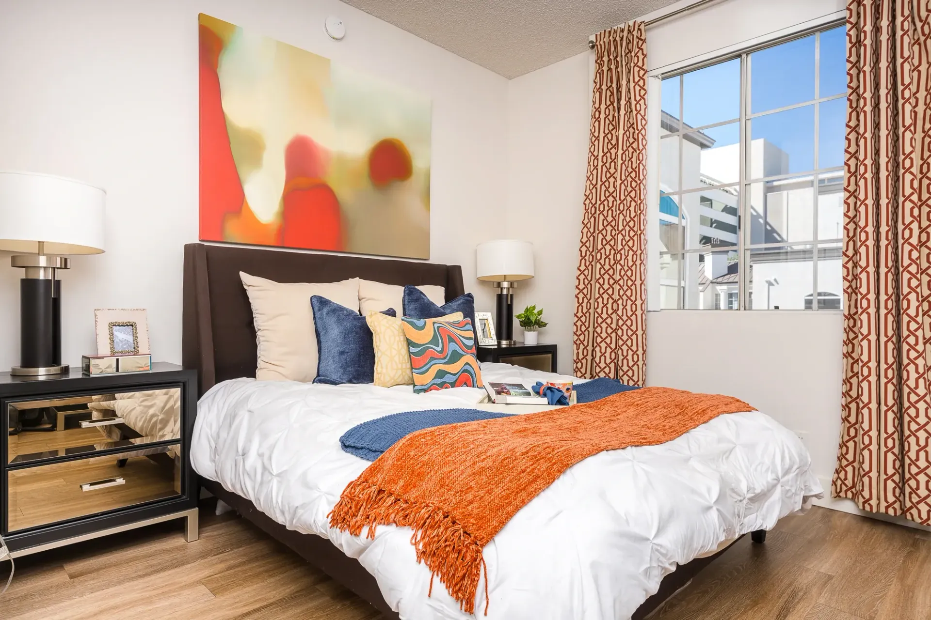 Bedroom with a queen-size bed, orange throw blanket, and abstract art at The Preston in Los Angeles, CA.