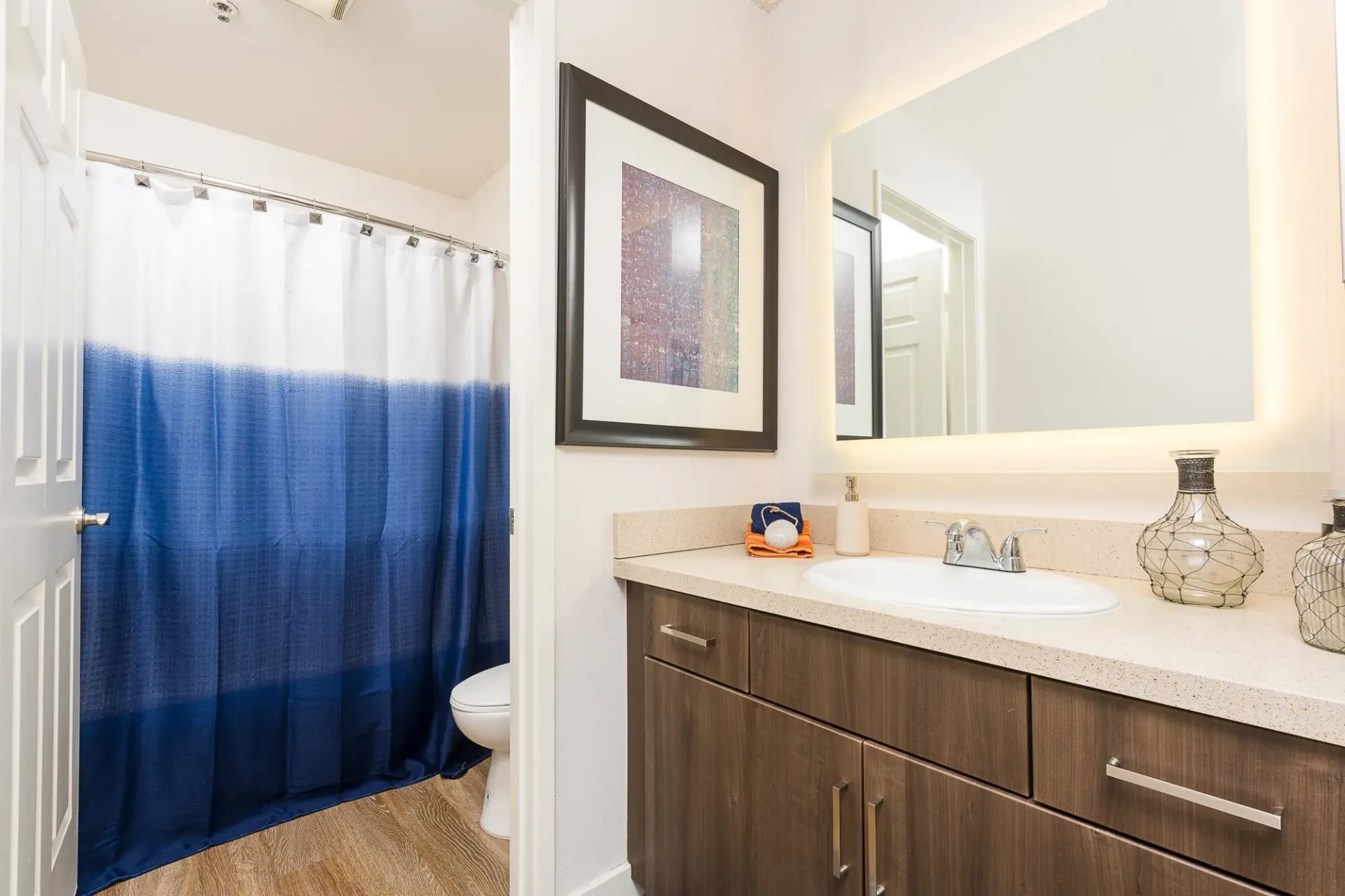 Modern bathroom with a blue gradient shower curtain, vanity, and illuminated mirror at The Preston in Los Angeles, CA.