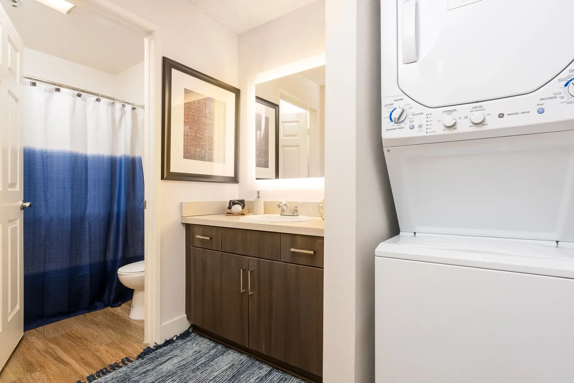Bathroom with vanity, stacked washer/dryer, and toilet behind shower curtain at The Preston in Los Angeles, CA.
