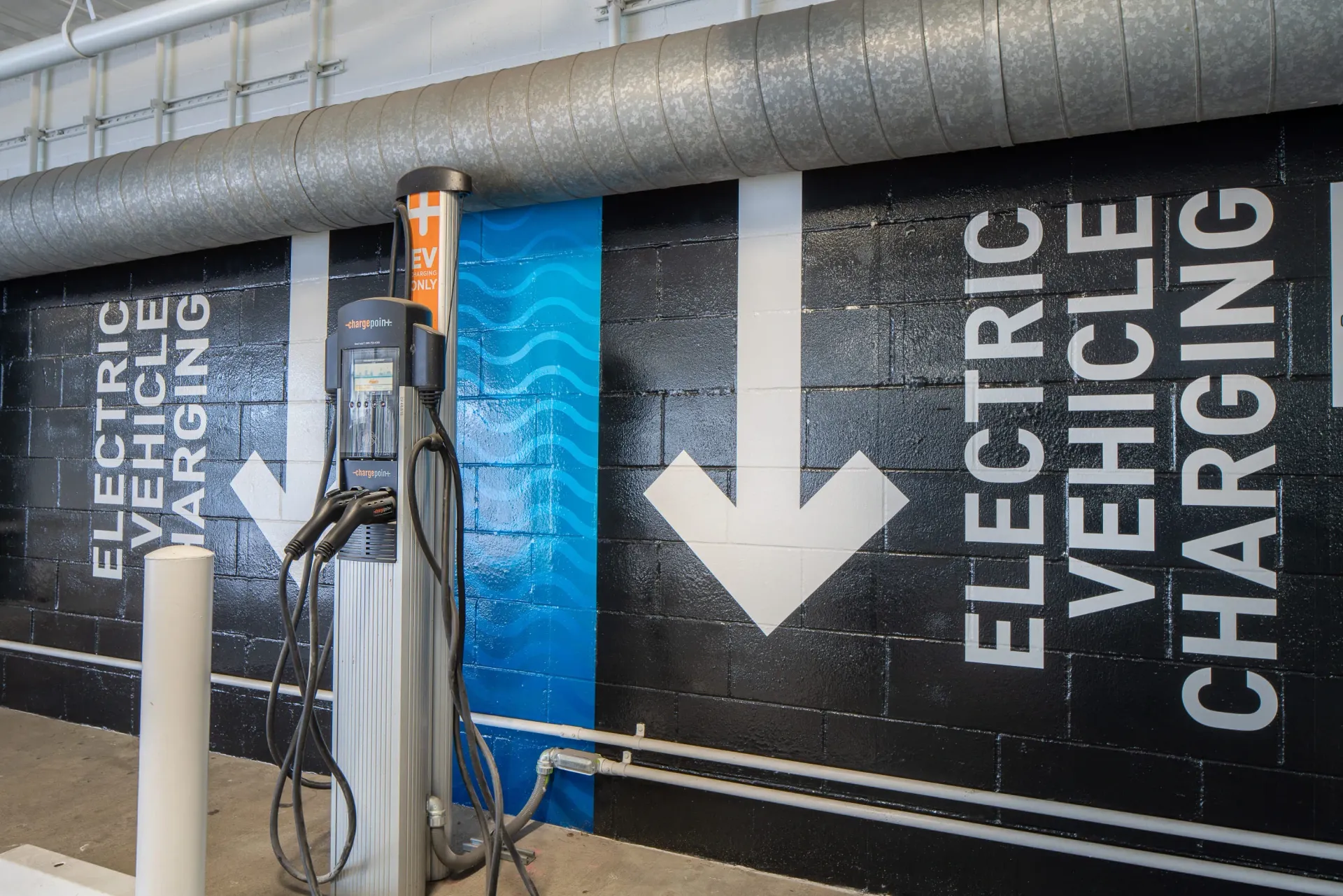 Electric vehicle charging station with directional arrows on a brick wall at The Preston in Los Angeles, CA.
