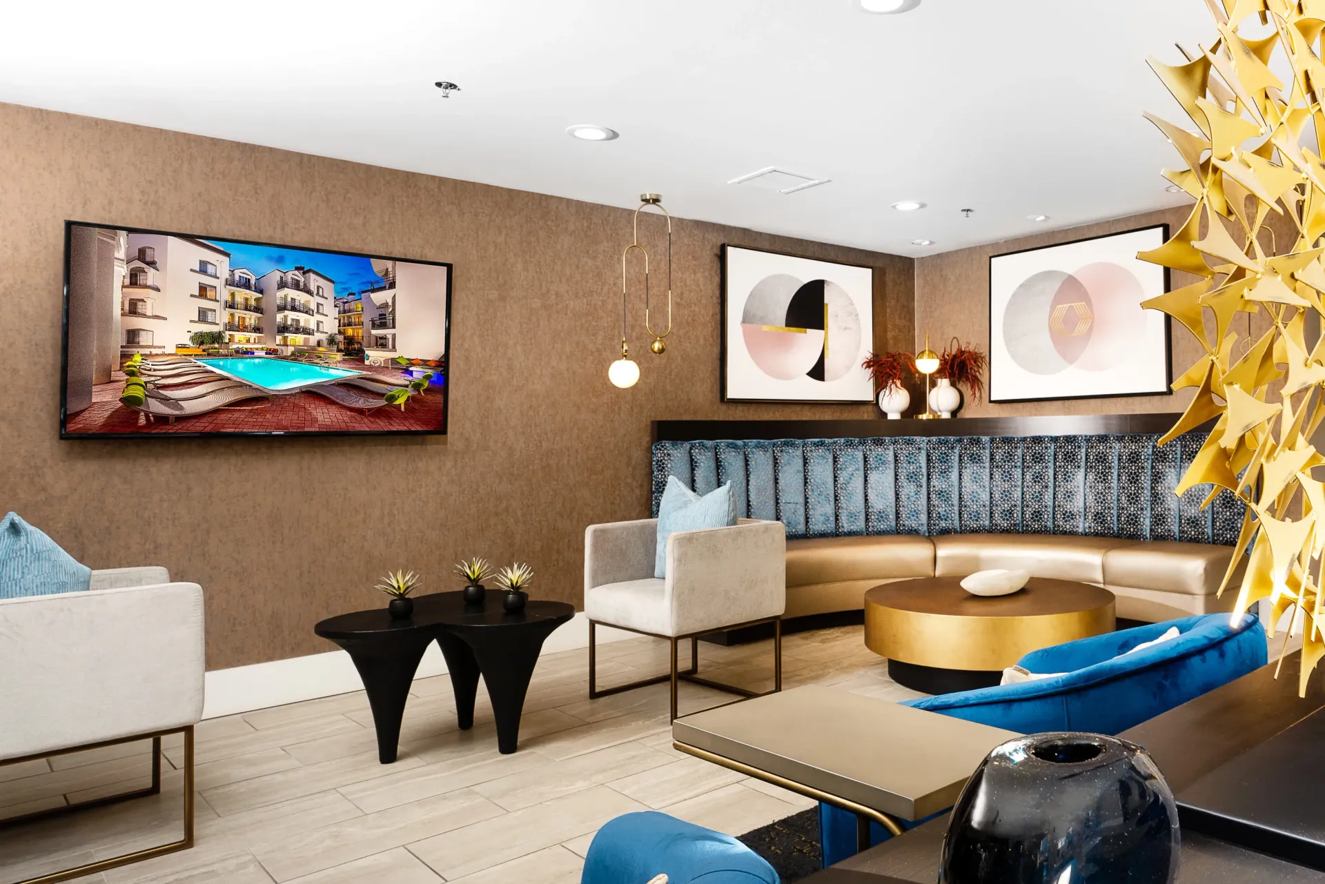 Lobby with seating and a TV displaying an image of a swimming pool and apartment buildings at The Preston in Los Angeles, CA.