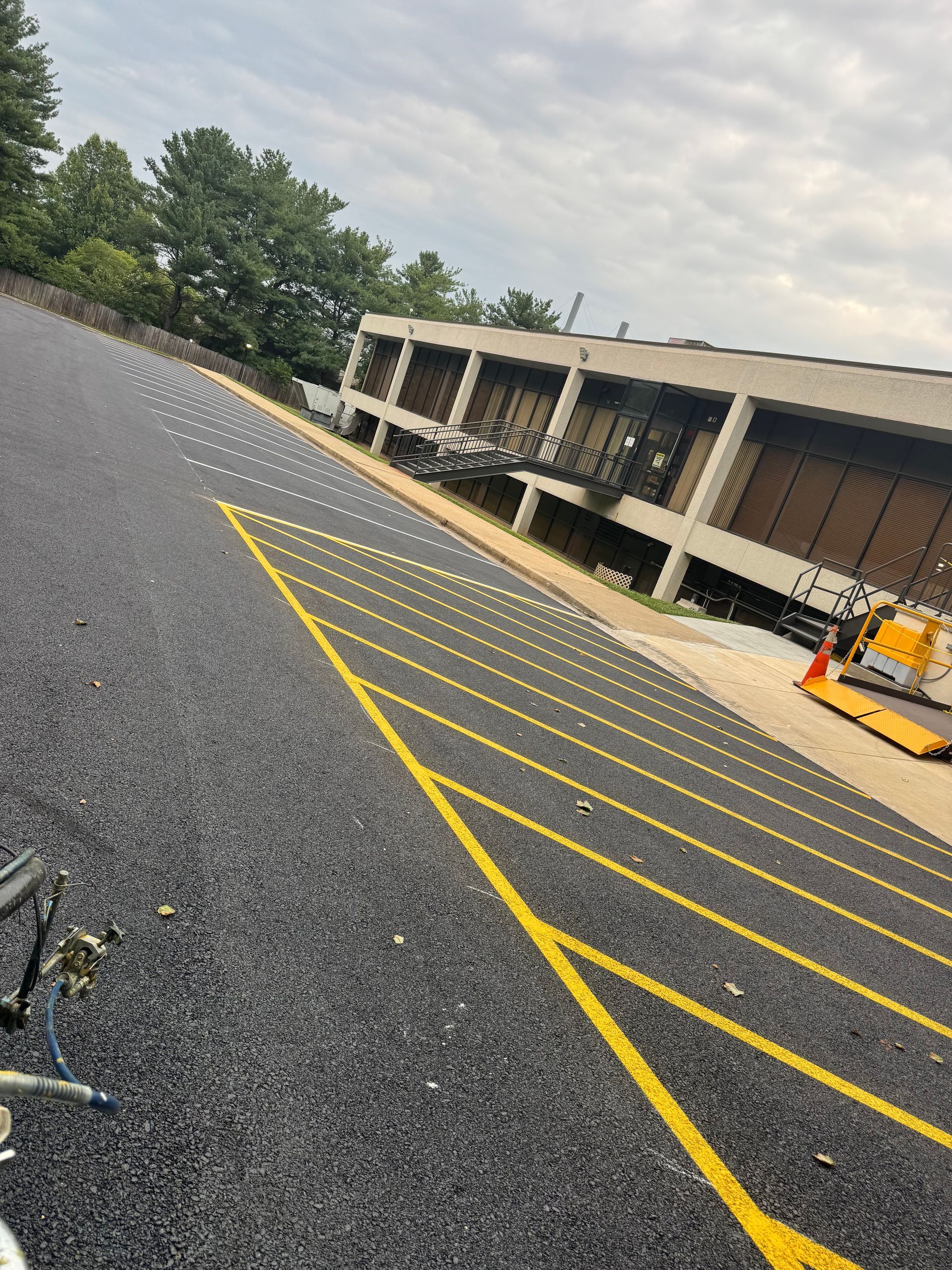 Empty parking lot with yellow lines beside a beige building and trees under a cloudy sky