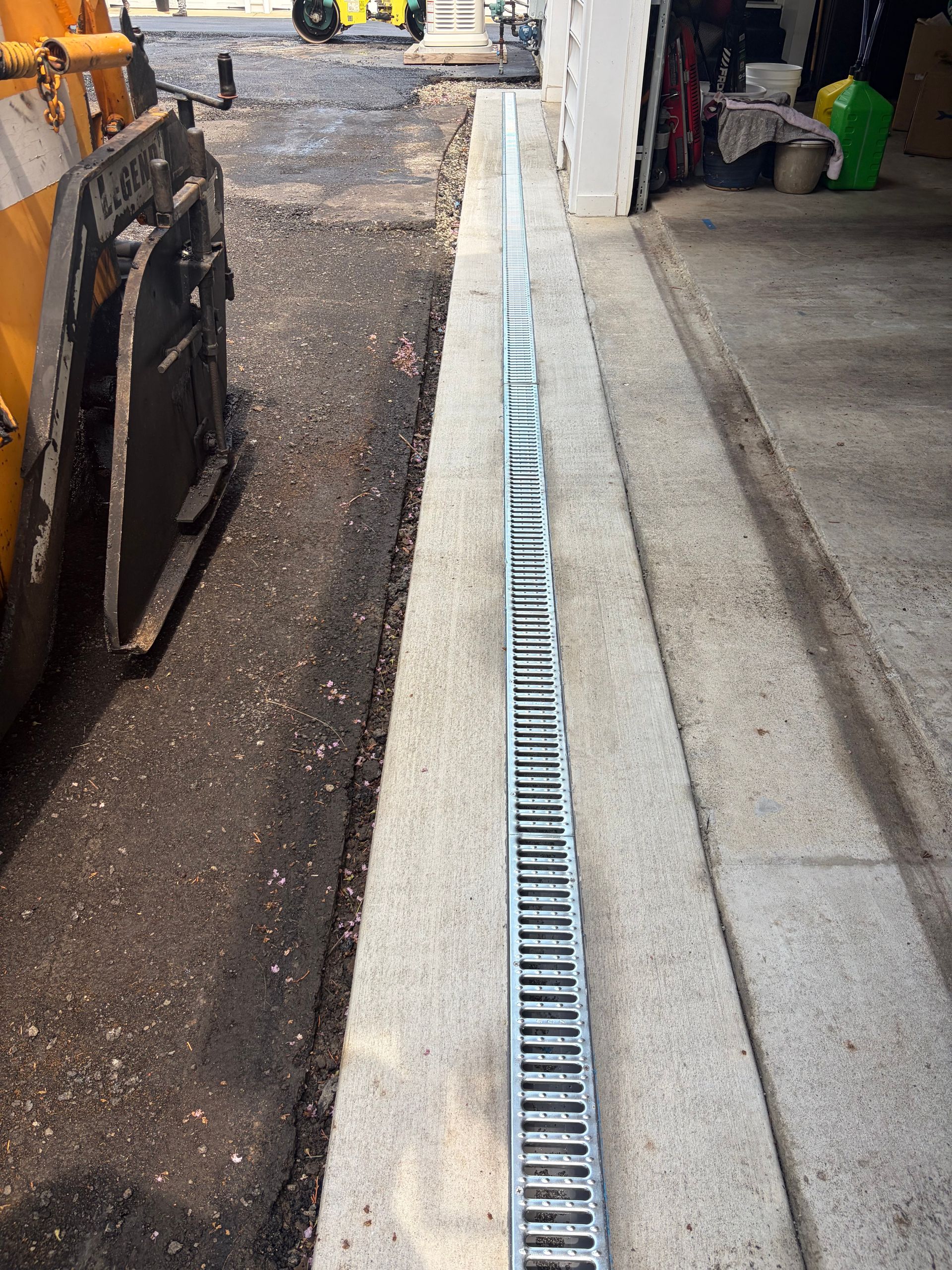 Construction site with trench drain alongside a concrete walkway next to a building.