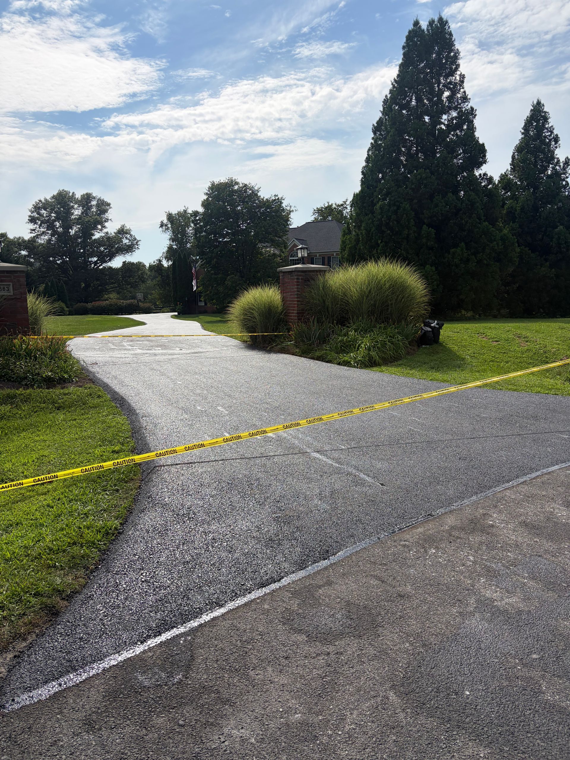 Gravel driveway blocked by yellow caution tape in a sunny suburban yard