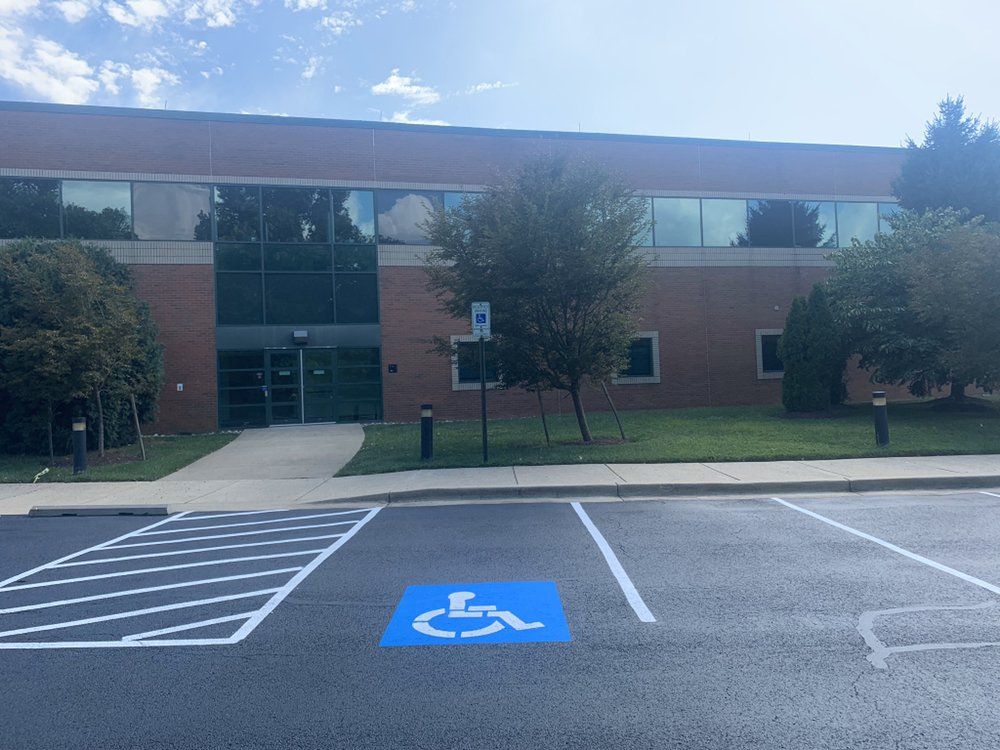 Accessible parking space in front of a brick building with a glass entrance and trees.