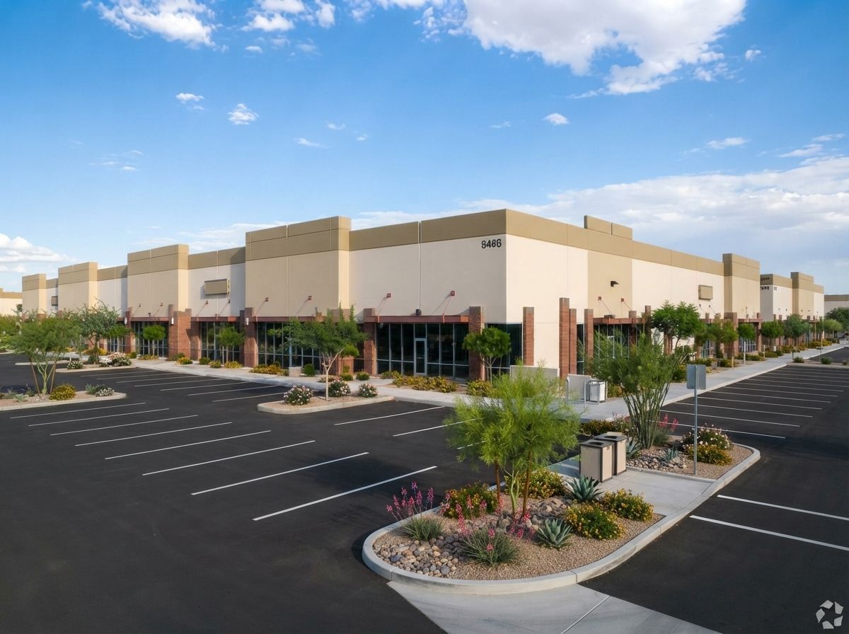 Large beige retail building with empty parking lot and landscaped entrance under a blue sky