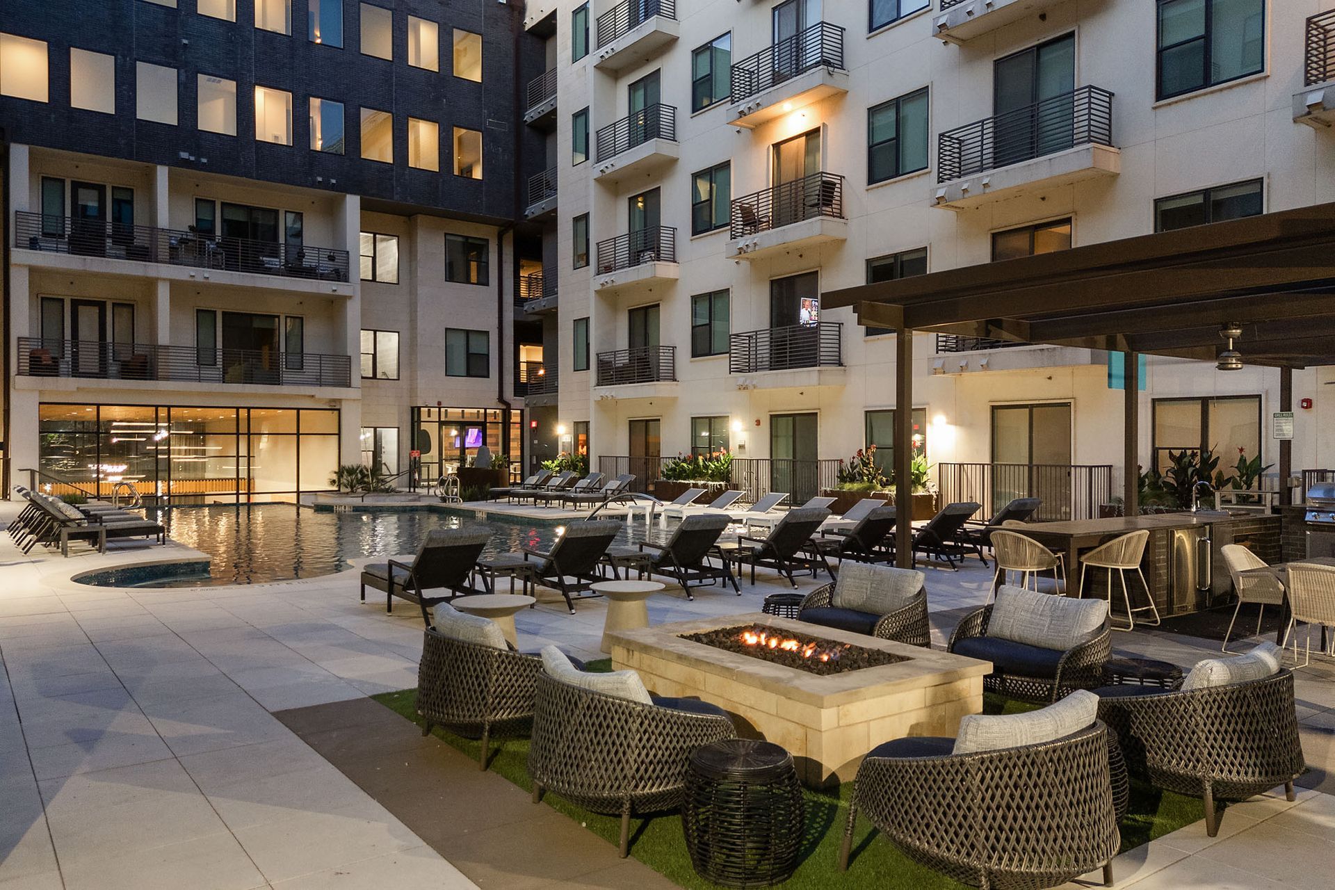 Outdoor hotel courtyard with lounge chairs, fire pit tables, and apartment balconies at dusk