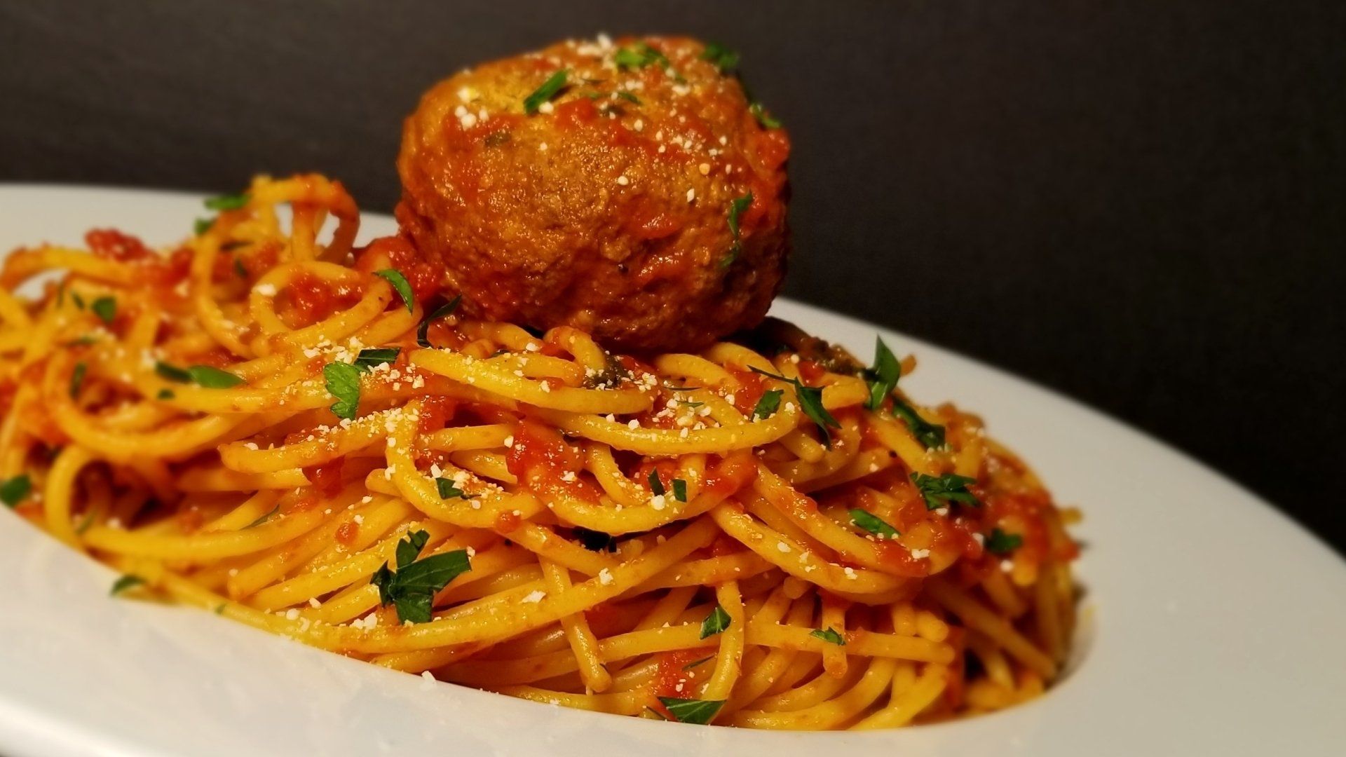 A plate of spaghetti and meatballs with a meatball on top.