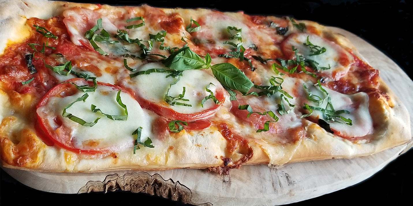 A pizza with tomatoes and cheese is sitting on a wooden cutting board.