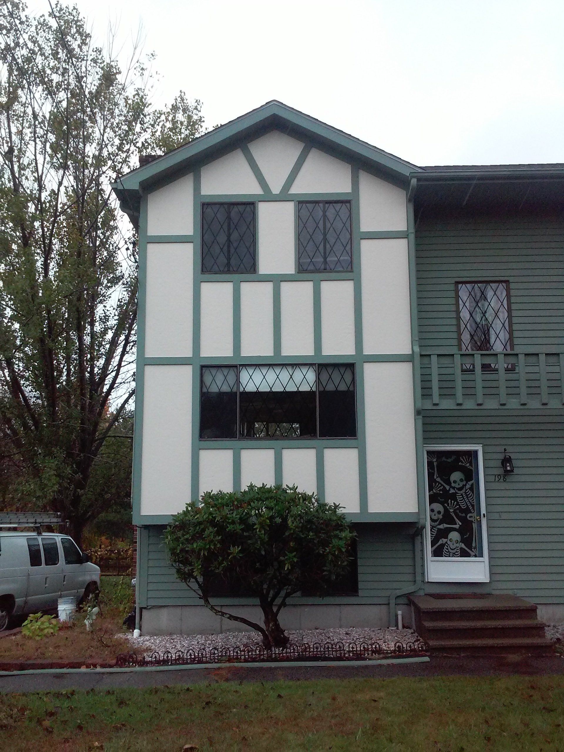 Two-story house with green siding and white and green Tudor-style trim. A small tree sits in front.
