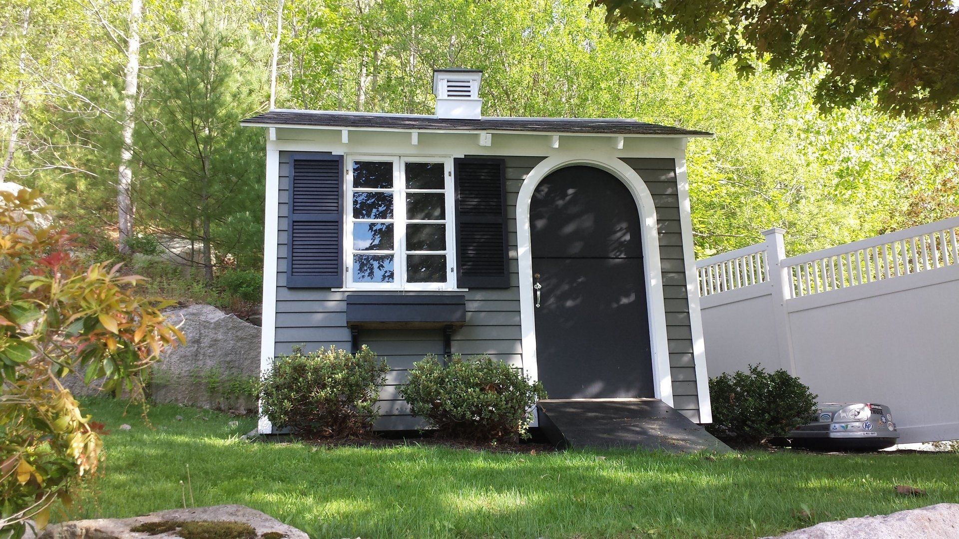Small gray and white shed with a window, door, and ramp, in a grassy yard.