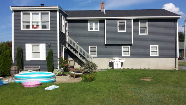 Backyard with dark gray house, wooden stairs, small pool, and green grass.