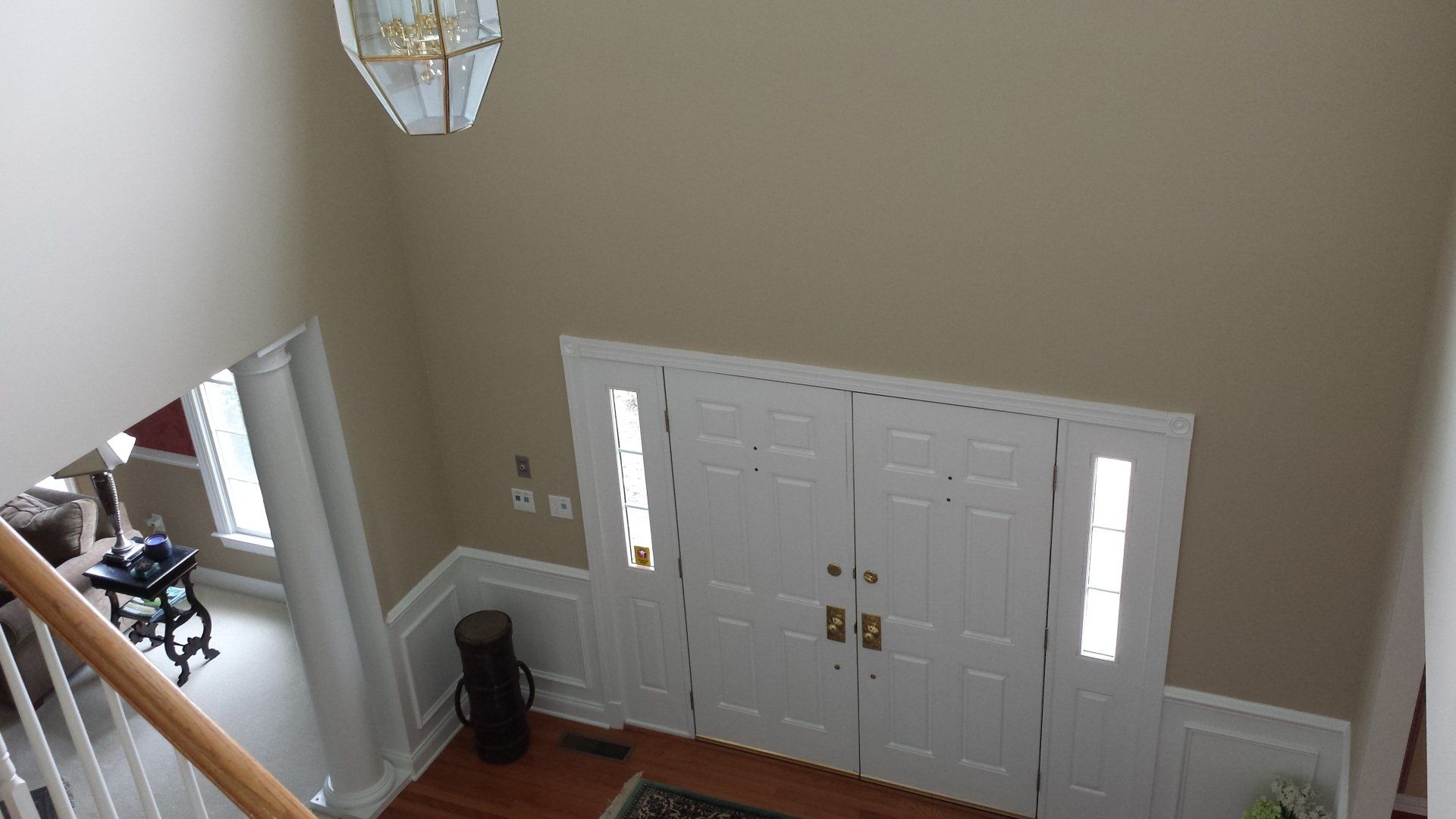 View from above of a two-story entryway with white double doors, sidelights, and tan walls.
