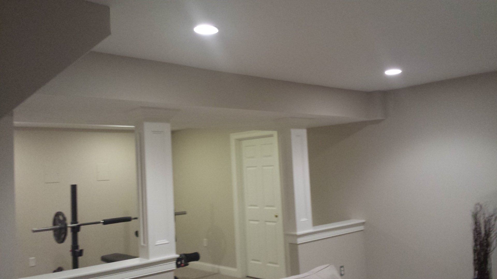 Basement with weight equipment, white columns, recessed lighting, and a closed door.