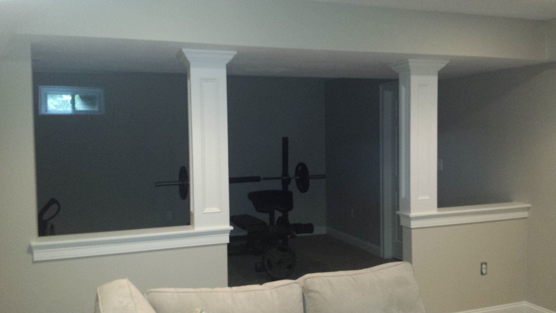 Basement workout area with pillars and weight bench visible through openings.