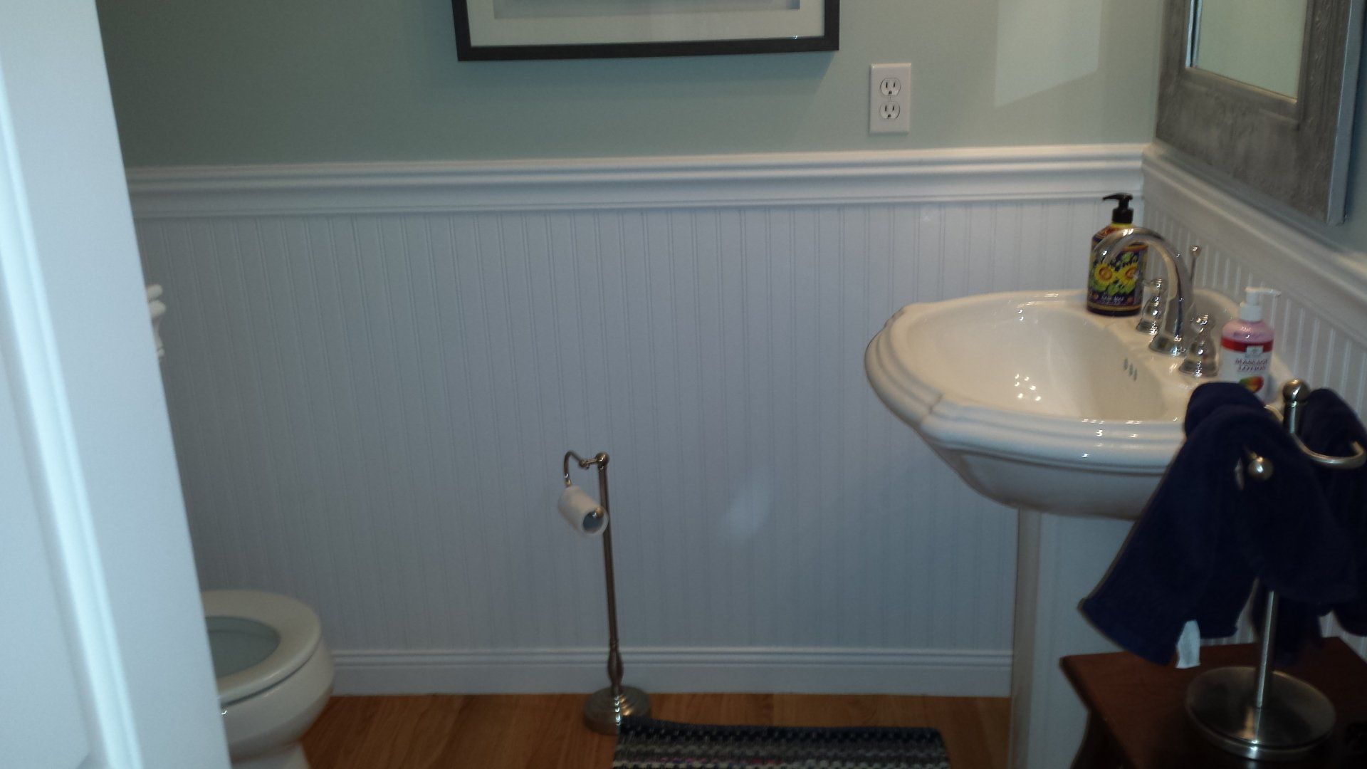 Small bathroom with pedestal sink, toilet, and beadboard paneling.