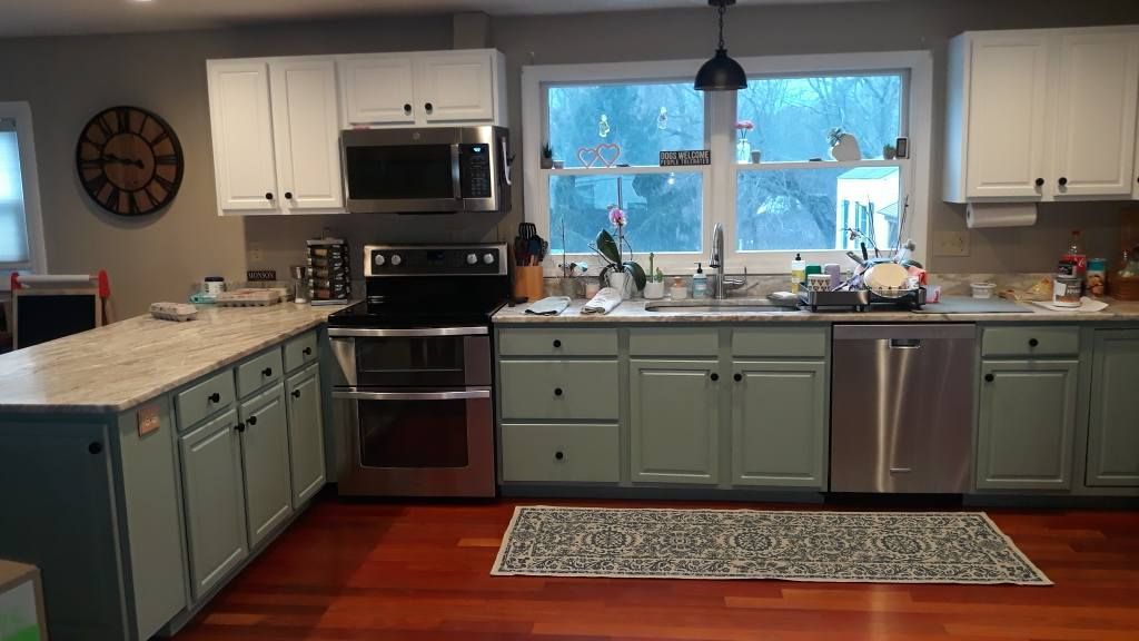Kitchen with sage green lower cabinets, white upper cabinets, stainless steel appliances, and a window over the sink.