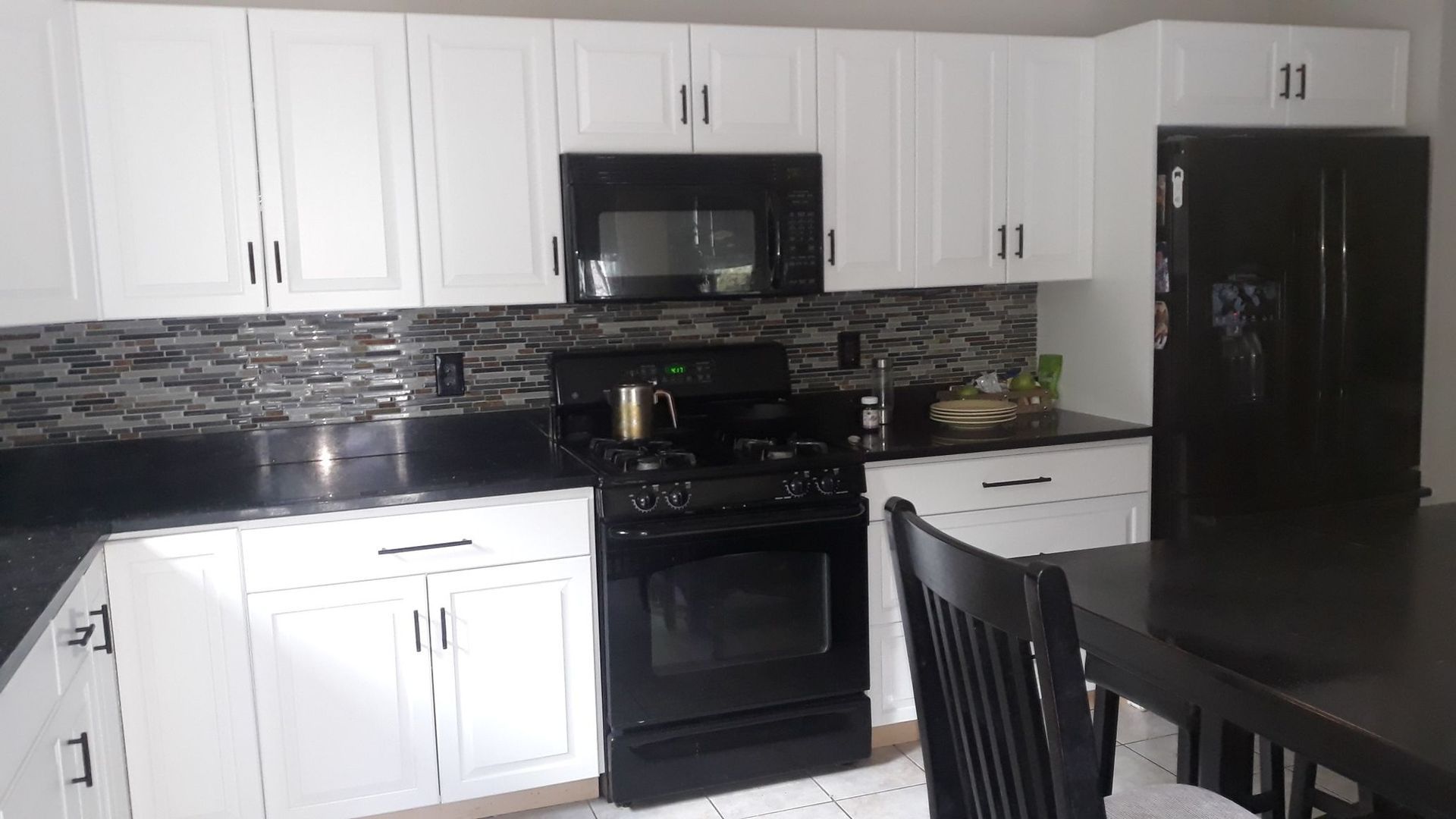 White kitchen cabinets with black appliances, counters, and backsplash.