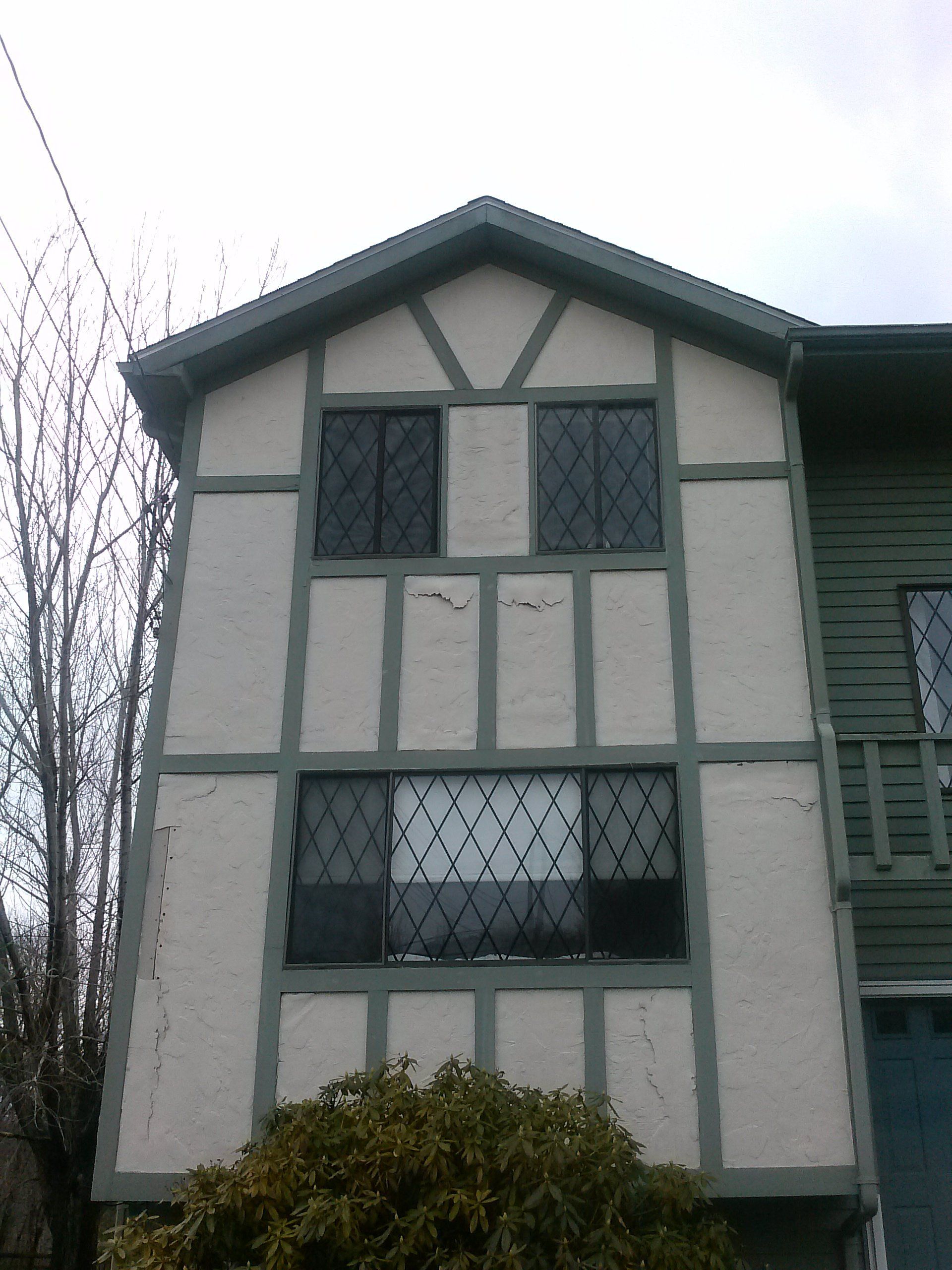 Tudor-style house with green trim and dark windows, two stories tall. White stucco and dark windows.