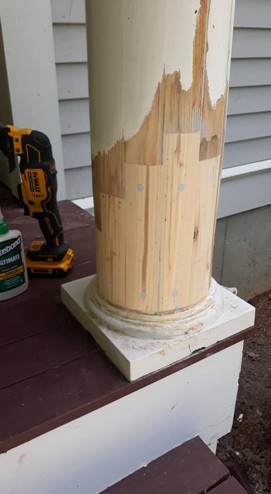 A white porch column with peeling paint and exposed wood, tools nearby, sitting on a white base.