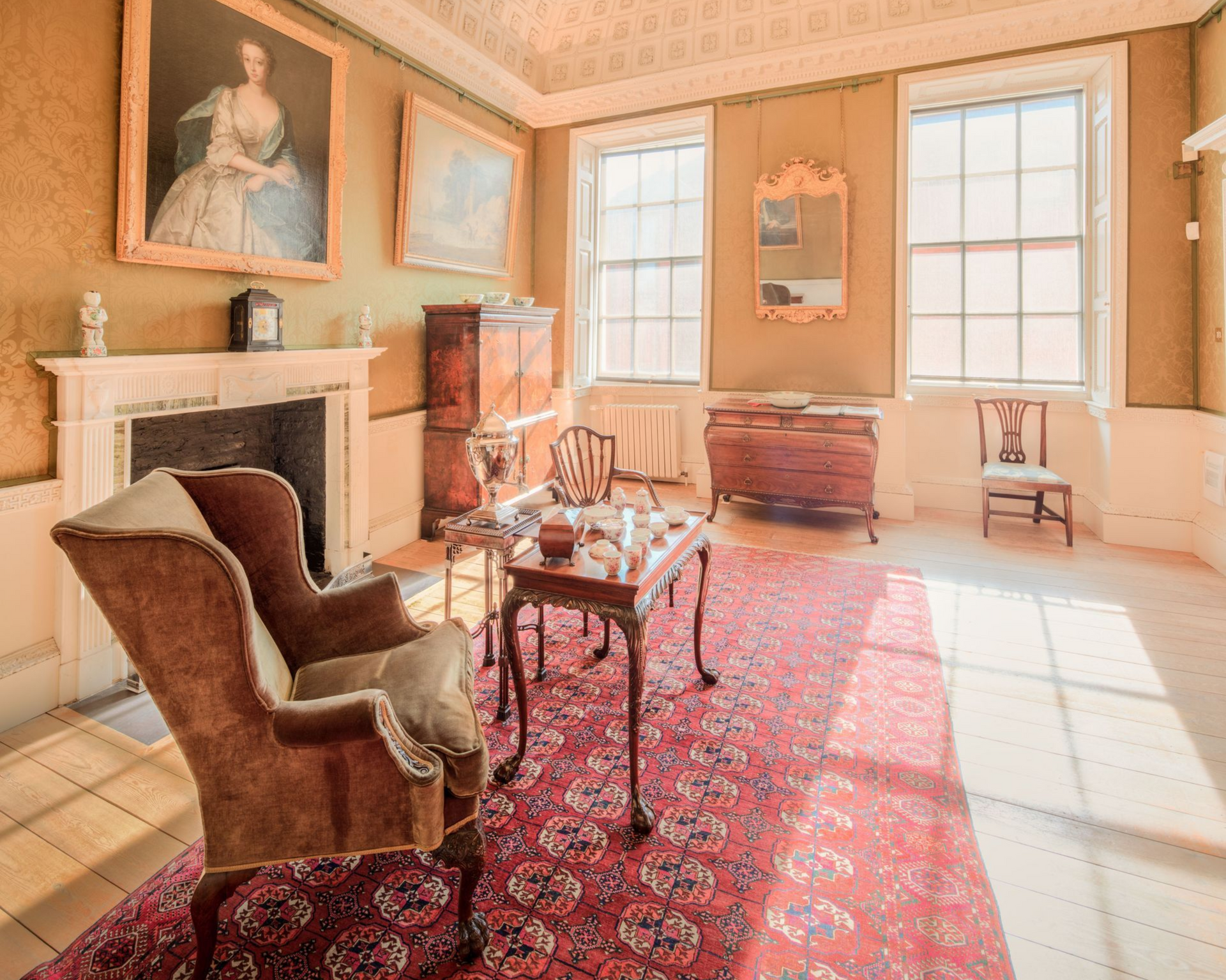 Elegant vintage sitting room with ornate ceiling, fireplace, red rug, and large windows