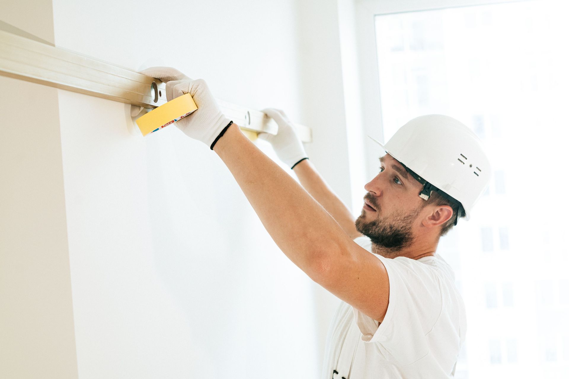 Worker in a white hard hat using a drill to install a fixture on a wall
