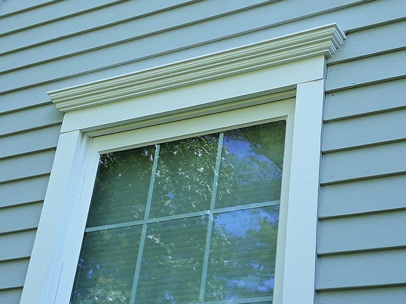 Window with white trim and decorative molding, set against light blue siding.