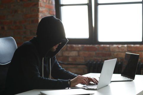 Un hombre con una sudadera con capucha está sentado en un escritorio usando una computadora portátil.