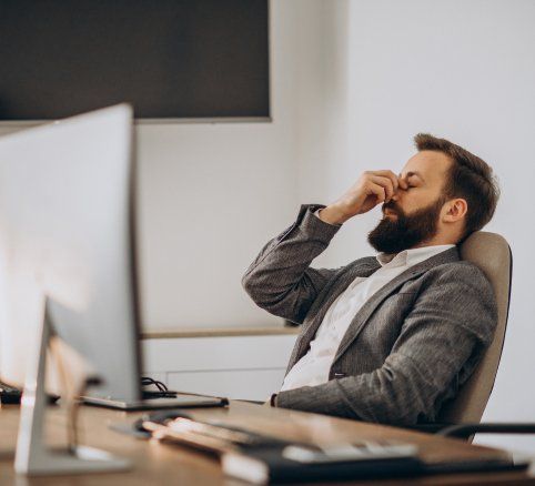 Un hombre con barba está sentado en un escritorio frente a una computadora.