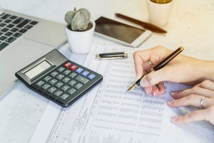 Una persona está escribiendo en un trozo de papel al lado de una calculadora.