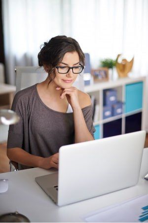 Una mujer con gafas está sentada en un escritorio utilizando una computadora portátil.