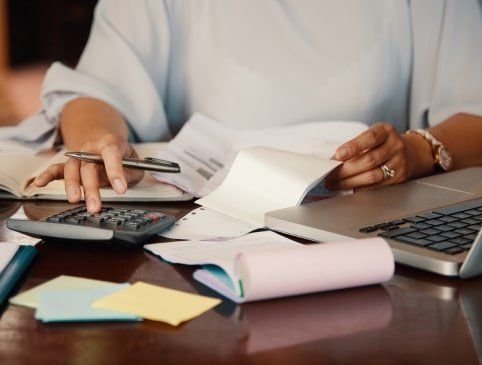 Una mujer está sentada en un escritorio con una computadora portátil y una calculadora.
