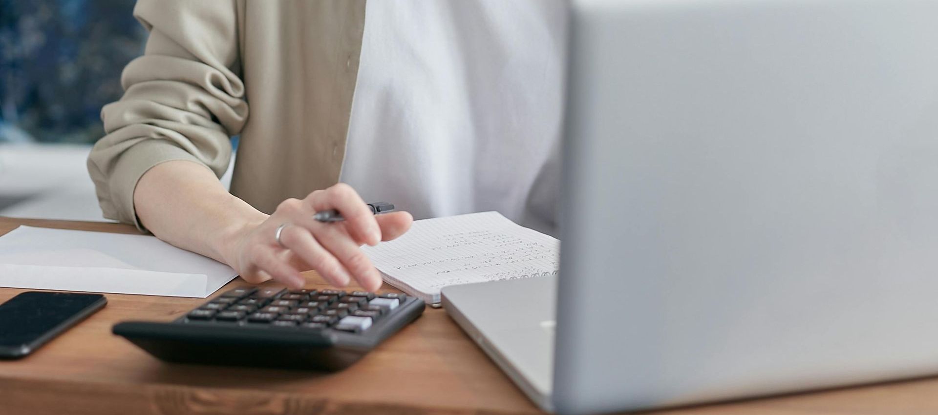 Una mujer está usando una calculadora frente a una computadora portátil.
