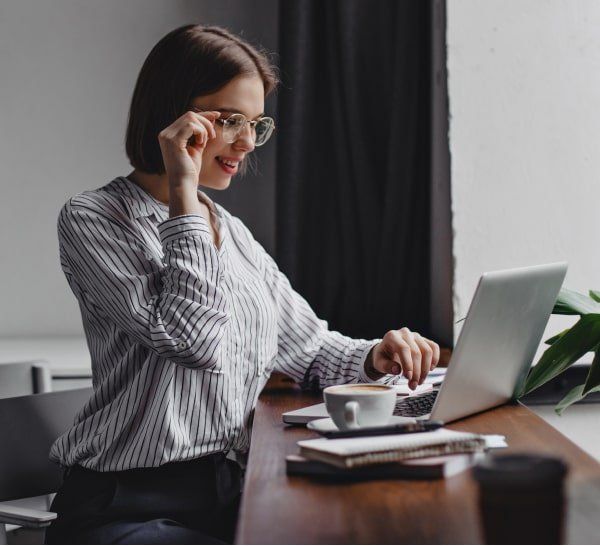 Una mujer está sentada en un escritorio usando una computadora portátil y hablando por un teléfono celular.