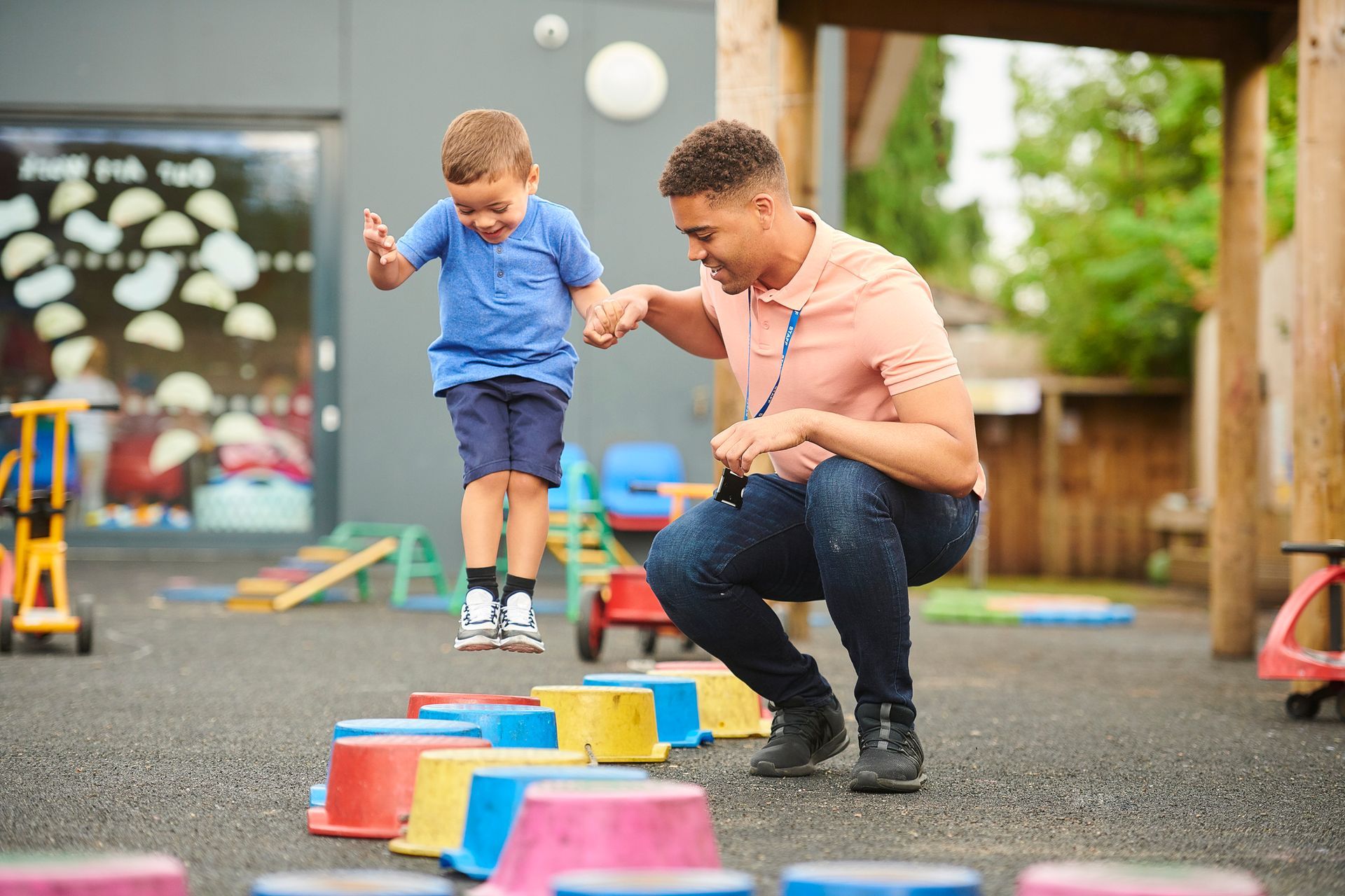 Child jumping colorful blocks with help from an adult in a playground setting.